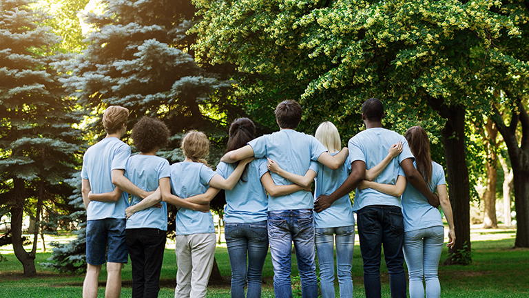 Volunteering, people and ecology concept. Group of volunteers embracing in park, back view, copy space