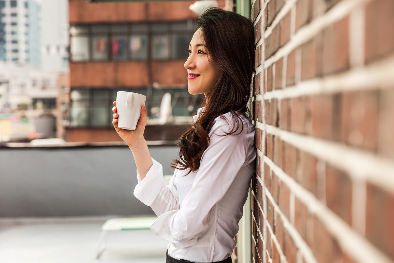 Young business woman having a break drinking an hot coffee on the rooftop of his office building in downtown Seoul, South Korea.