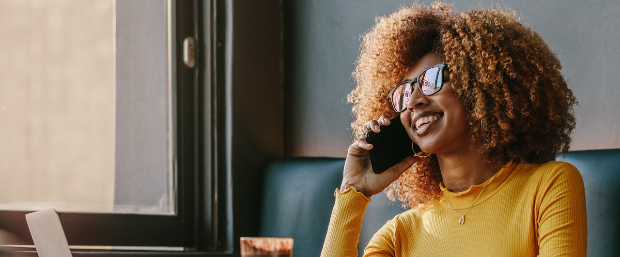 Freelance businesswoman working on laptop sitting at a restaurant and talking on cell phone. Woman sitting in a coffee shop talking on phone with laptop and snacks on table.